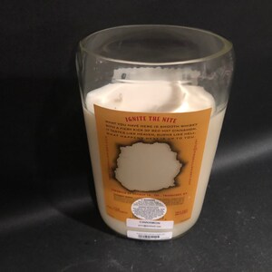 May include: A clear glass candle jar with a white candle inside. The candle is labeled "Ignite the Nite" and has a description that reads "What you have here is smooth whiskey with a fiery kick of red hot cinnamon. It tastes like heaven, burns like hell. What happens next is up to you."