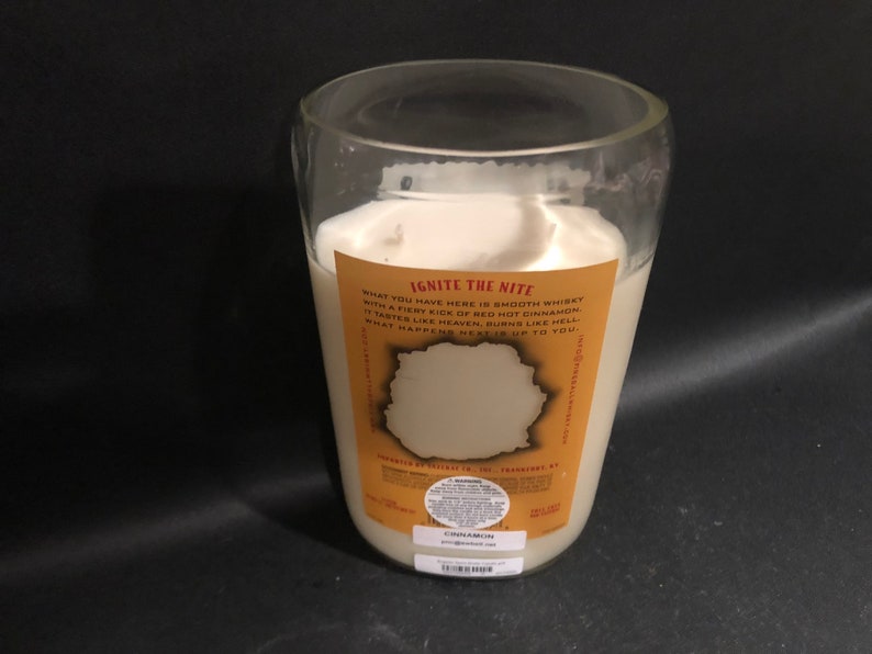 May include: A clear glass candle jar with a white candle inside. The candle is labeled "Ignite the Nite" and has a description that reads "What you have here is smooth whiskey with a fiery kick of red hot cinnamon. It tastes like heaven, burns like hell. What happens next is up to you."