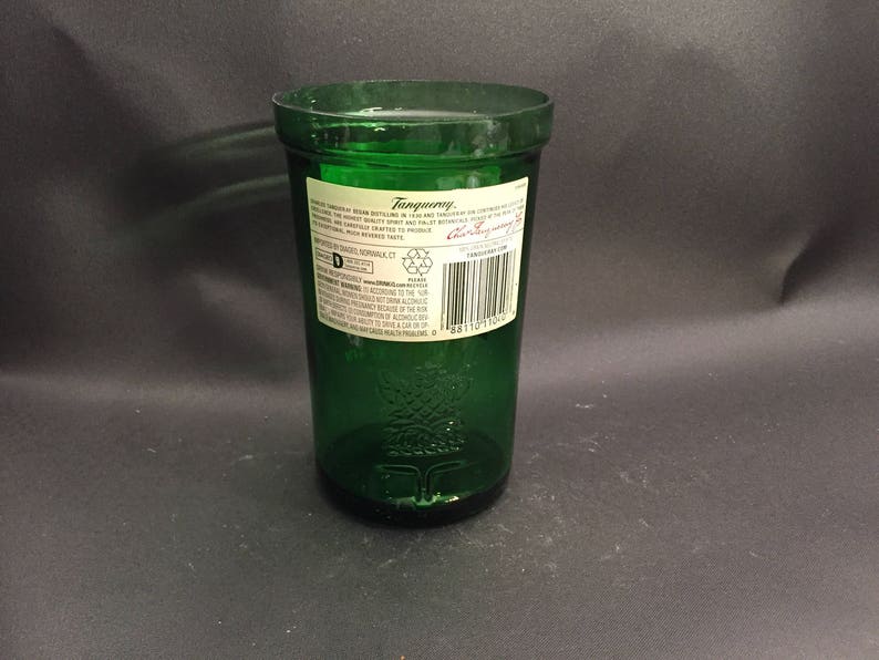 May include: A green glass bottle with a label that reads "Tanqueray" and "London Dry Gin". The bottle is empty and has a textured surface.