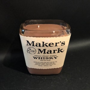 May include: A brown candle in a clear glass bottle with a Maker's Mark whiskey label. The label reads "Maker's Mark Kentucky Straight Bourbon Whisky Handmade Distilled, Aged and Bottled by the Maker's Mark Distillery Inc. Star Hill Farm, Loretto, KY USA 45% Alc./Vol."