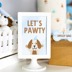 May include: White sign with a blue background and the text "Let's Pawty" in brown letters. A cartoon dog wearing a blue party hat is in the center of the sign.