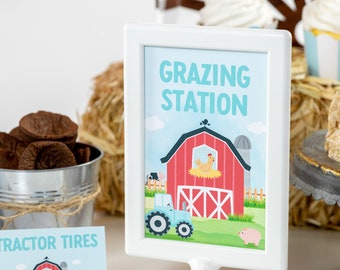 Könnte beinhalten: Ein weißer Bilderrahmen mit einem blauen und grünen Schild, auf dem "Grazing Station" steht. Das Schild zeigt einen roten Cartoon-Stall mit einem Huhn darin, einen blauen Traktor, eine Kuh und ein Schwein.