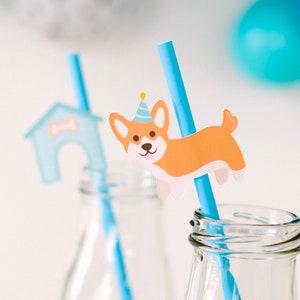 May include: Two clear glass bottles with blue and white striped straws. One straw has a paper cutout of a dog wearing a party hat, the other has a paper cutout of a dog house.