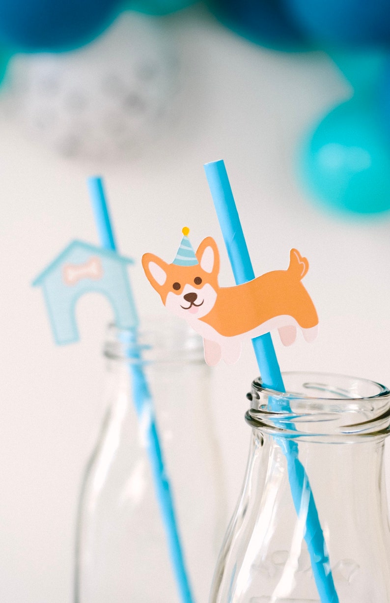 May include: Two clear glass bottles with blue and white striped straws. One straw has a paper cutout of a dog wearing a party hat, the other has a paper cutout of a dog house.