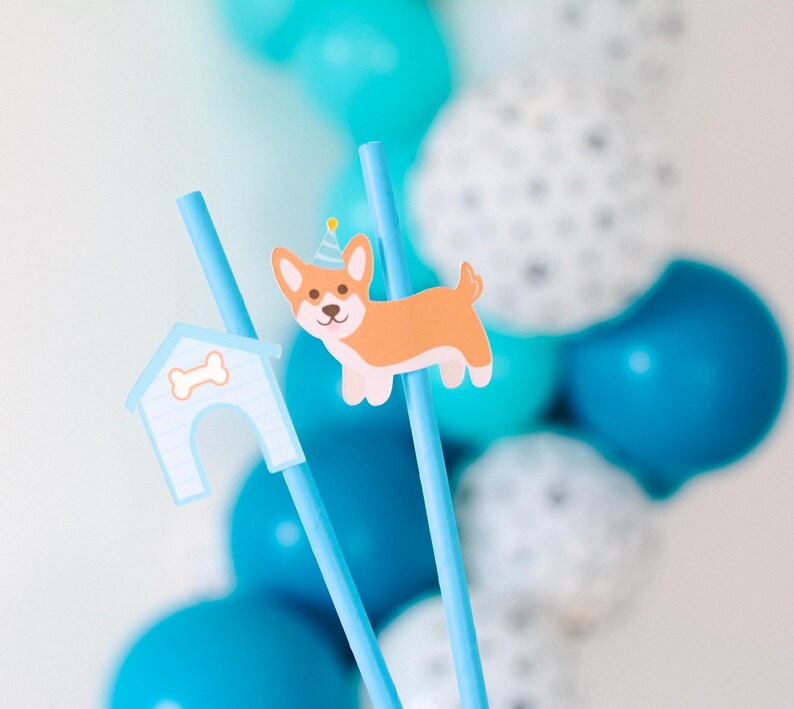May include: Two blue straws with a dog house and a dog wearing a party hat attached. The straws are in front of a background of blue and white balloons.