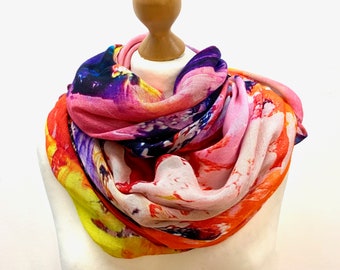 May include: A colorful scarf with a floral print in shades of pink, orange, yellow, and purple. The scarf is draped around a mannequin's neck.