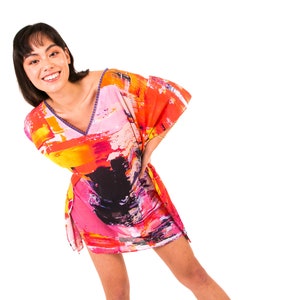 May include: A woman wearing a colorful abstract print kaftan with a V-neckline. The kaftan is made of a lightweight fabric and has a relaxed fit.
