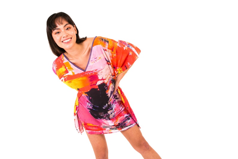 May include: A woman wearing a colorful abstract print kaftan with a V-neckline. The kaftan is made of a lightweight fabric and has a relaxed fit.