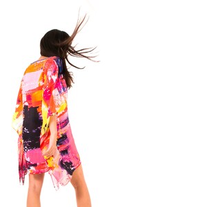 May include: A woman wearing a colorful, abstract print kaftan with long sleeves. The kaftan is flowing in the wind, and the woman's hair is blowing in the wind.