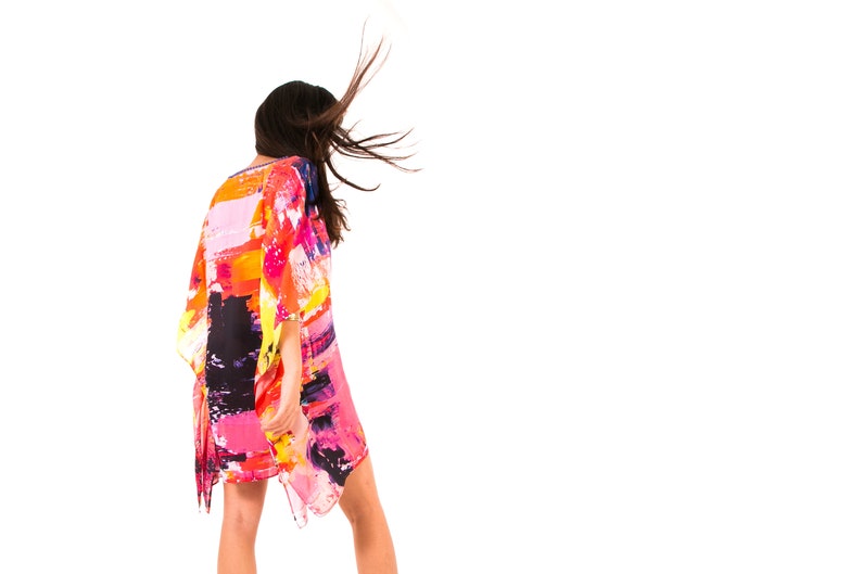 May include: A woman wearing a colorful, abstract print kaftan with long sleeves. The kaftan is flowing in the wind, and the woman's hair is blowing in the wind.
