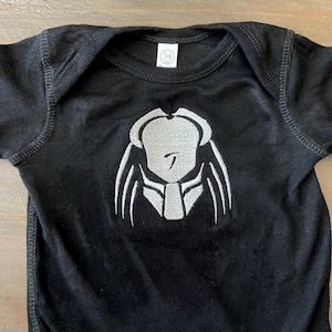 May include: Black baby onesie with a white embroidered Predator head.