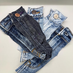 May include: A collection of denim fabric scraps in various shades of blue, including light blue, medium blue, and dark blue. The fabric scraps are arranged in a pile, with the edges of the fabric visible.