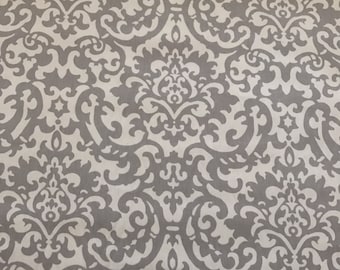 May include: A white fabric with a gray damask pattern. The pattern features intricate swirls and floral designs.