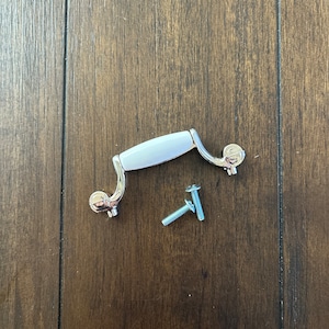 May include: A white ceramic drawer pull with a silver finish and two screws.