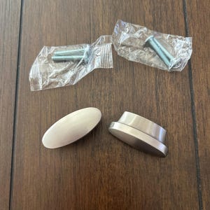 May include: Two brushed nickel oval cabinet knobs with two sets of screws in plastic packaging.