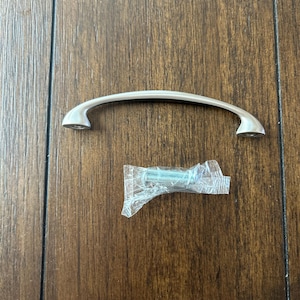 May include: A silver cabinet pull with a curved shape and rounded ends. The pull comes with two screws in a plastic bag.