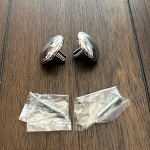 May include: Two silver cabinet knobs with a rounded top and a short stem. Two silver screws are included in separate plastic bags.