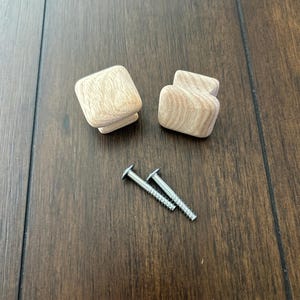 May include: Two wooden square cabinet knobs with a light brown finish and two silver screws.