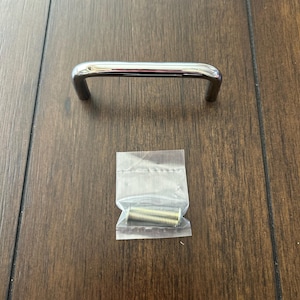 May include: A chrome cabinet pull with a rounded rectangular shape. The pull comes with two gold screws.