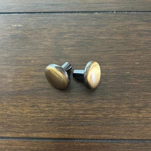 May include: Two round, brass cabinet knobs with a black metal base. The knobs have a slightly aged, antique finish.
