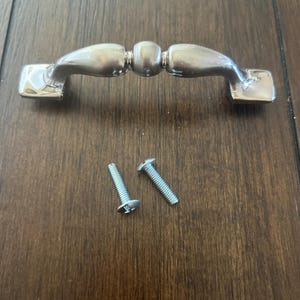 May include: A silver cabinet knob with a rounded design and two screws.
