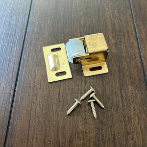 May include: A gold-toned door catch with a white roller and a strike plate. The catch comes with four screws.