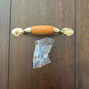 May include: A wooden cabinet knob with a gold metal base. The knob is brown and has a rounded shape. The knob comes with two screws for installation.