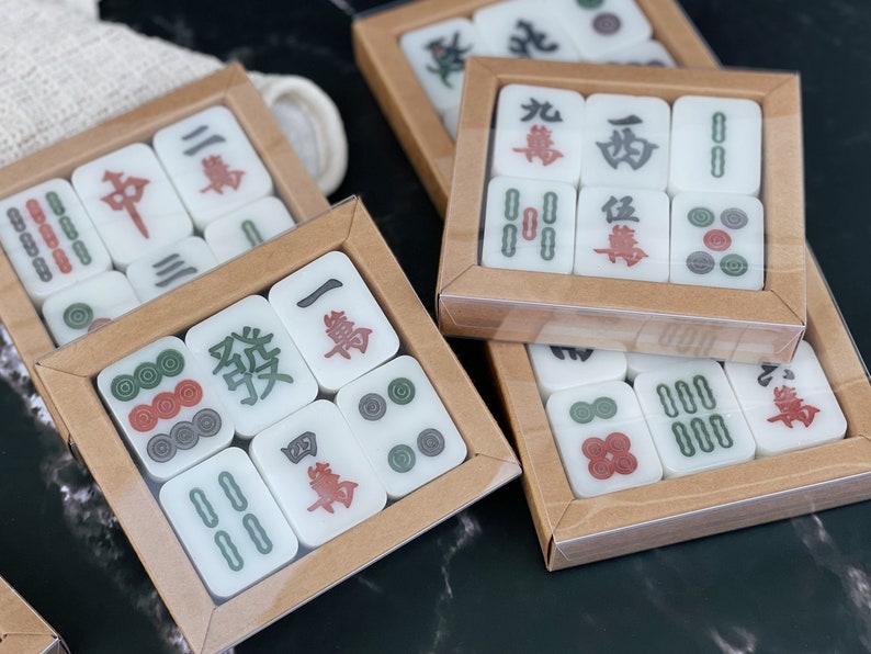 May include: A set of mahjong tiles in a wooden box. The tiles are white with black and red characters and symbols. The box is brown with a clear plastic lid.