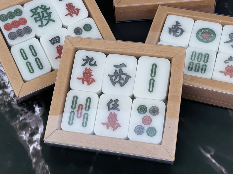 May include: A set of white mahjong tiles with Chinese characters and red and green dots. The tiles are arranged in a rectangular box with a brown wooden frame.