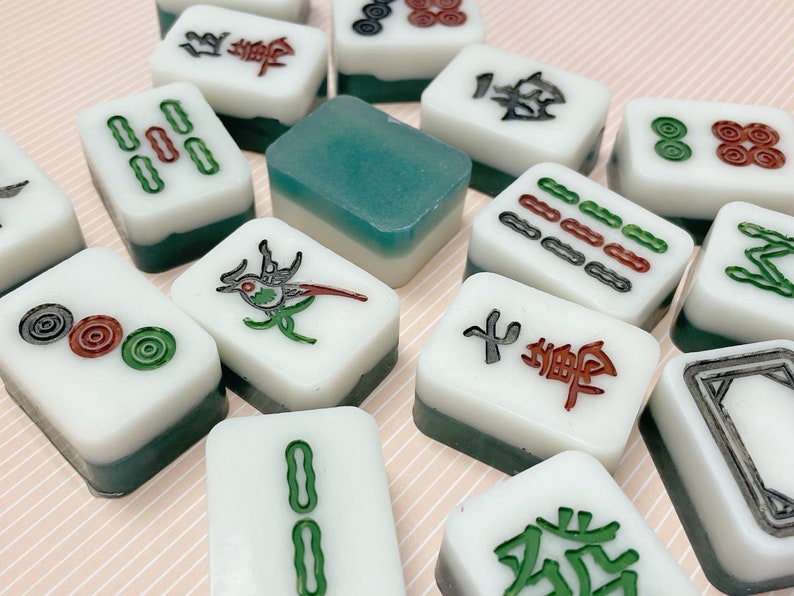 May include: A collection of green and white Chinese dominoes with various symbols and numbers. The dominoes are arranged in a random pattern on a light brown surface.