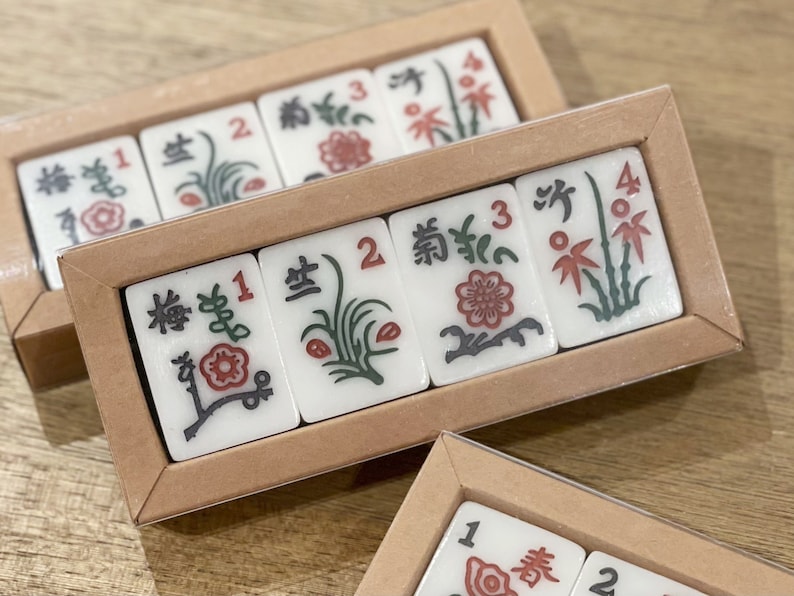 May include: A set of six white ceramic tiles with black and green floral designs and red flowers. The tiles are numbered 1, 2, 3, and 4. The tiles are arranged in a rectangular wooden box with a brown lid.