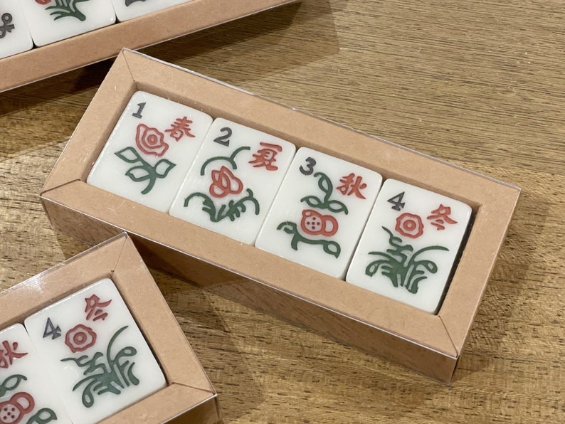 May include: Four white tiles with red and green floral designs and Chinese characters. The tiles are arranged in a row in a clear plastic case with a brown cardboard backing. The tiles are numbered 1 through 4.