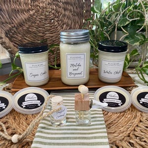 May include: Three glass jar candles with black lids, four oval wax melts, and two small glass fragrance diffusers with wooden caps. The candles feature labels reading Flickers, Sugar Cedar, Matcha and Bergamot, and Winter Chalet.