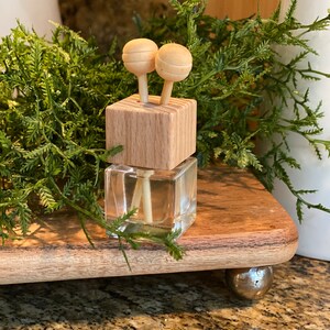 May include: A small glass bottle with a wooden lid and two wooden sticks. The bottle is filled with a clear liquid and the sticks are inserted into the lid. The bottle is sitting on a wooden surface.