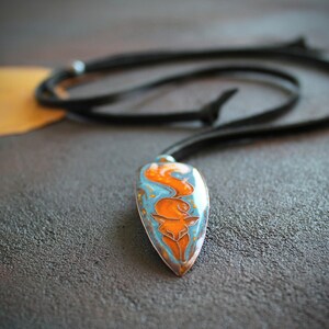 May include: A blue and orange enamel pendant with a fox design, hanging from a black leather cord.
