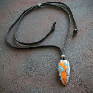 May include: A necklace with a leather cord and a pendant shaped like a teardrop. The pendant is made of ceramic and has a blue and orange design.