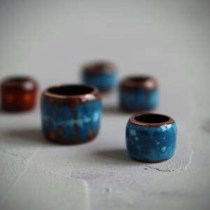 May include: Five ceramic beads in various shades of blue and brown. The beads are round and have a smooth, glossy finish.