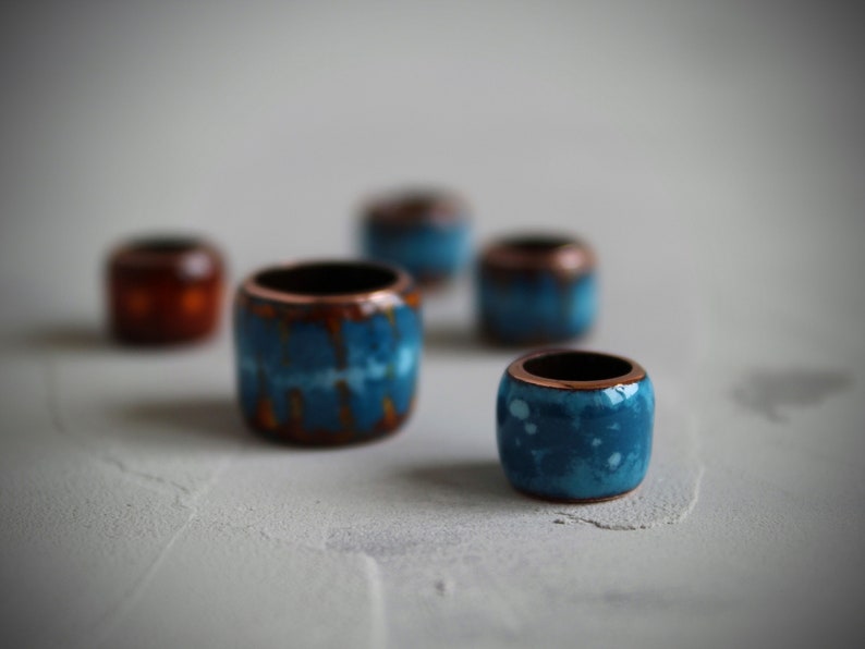 May include: Five ceramic beads in various shades of blue and brown. The beads are round and have a smooth, glossy finish.