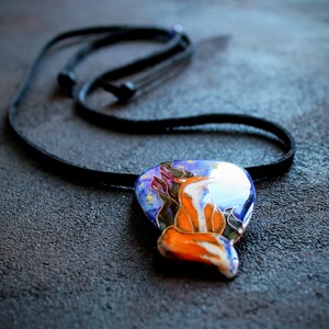 K&ouml;nnte beinhalten: Eine Halskette mit einem blauen, orangefarbenen und wei&szlig;en Anh&auml;nger, der ein stilisiertes Fuchsdesign zeigt. Der Anh&auml;nger ist vor einem Hintergrund aus Sternen und einem dunkelblauen Himmel platziert.