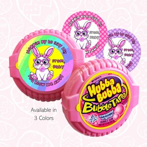 May include: Pink Hubba Bubba Bubble Tape with three circular stickers featuring a cartoon bunny wearing glasses and blowing a bubble. The stickers say "Hoppin by to say Hi! From, Ruby, You blow me away". The text "Available in 3 Colors" is also visible.