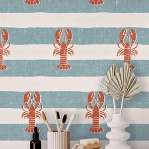 May include: Wallpaper featuring a repeating pattern of orange lobsters on horizontal blue and white stripes. In front, a dark amber glass bottle, a ribbed ceramic toothbrush holder with four brushes, a wooden brush, and a white vase.