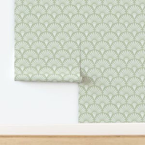 Peut inclure: Un rouleau de papier peint vert sauge avec un motif de ventilateur blanc répété. Le papier peint est partiellement déroulé, révélant le motif et la texture. Le design rappelle le style Art Déco.