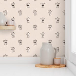 May include: Cream wallpaper featuring a repeating pattern of black coffee pots. A white ceramic jug, a small pink cup, and a wooden tray sit on a white countertop. A small wooden shelf holds a white mug.