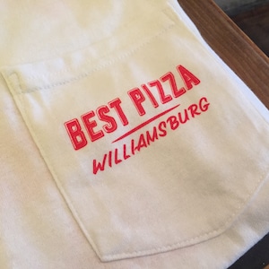 May include: White t-shirt with a red pocket that says "BEST PIZZA WILLIAMS BURG" in red.