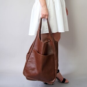 May include: A large brown leather tote bag with a large pocket on the front. The bag has a slouchy, unstructured look.