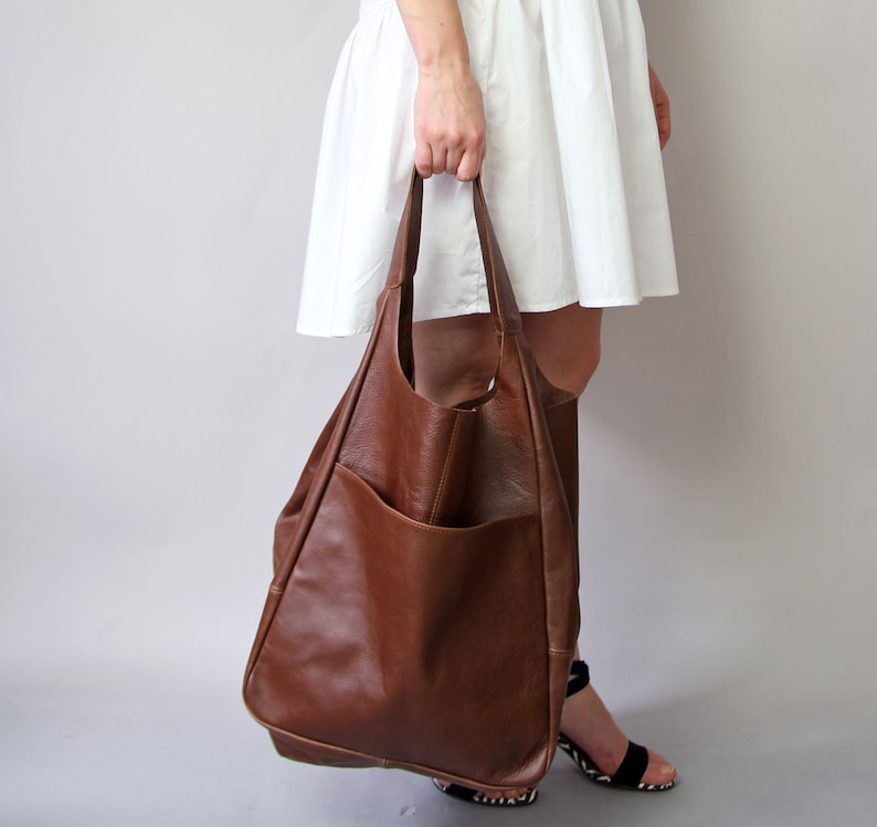May include: A large brown leather tote bag with a large pocket on the front. The bag has a slouchy, unstructured look.