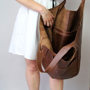 May include: A large brown leather tote bag with a zippered pocket on the inside. The bag is open and the inside is lined with brown suede.