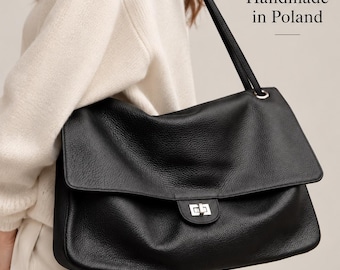 Puede incluir: Un bolso de hombro negro de cuero con superficie texturizada, solapa plegable y cierre giratorio de metal plateado. El bolso cuenta con una correa larga para el hombro e incluye el texto Handmade in Poland impreso en la parte superior derecha.