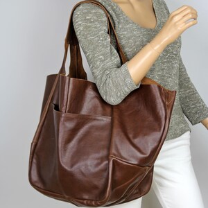 May include: A large brown leather tote bag with a single pocket on the front. The bag has a slouchy, relaxed look and is made of high-quality leather.