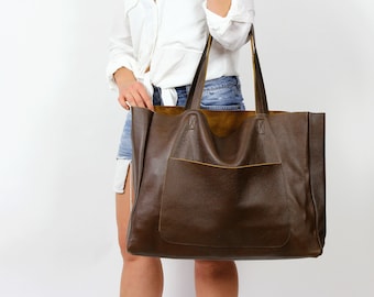 May include: A large brown leather tote bag with a smaller pocket on the front. The bag has a brown leather lining and two top handles.